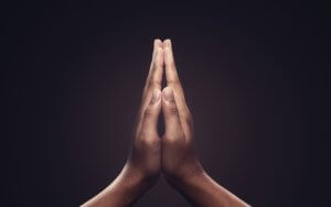 Close-up of two hands pressed together in a prayer-like gesture against a dark background. The fingers are straight and the palms are touching, creating a symmetrical and peaceful image, symbolizing the serenity and reverence for life.
