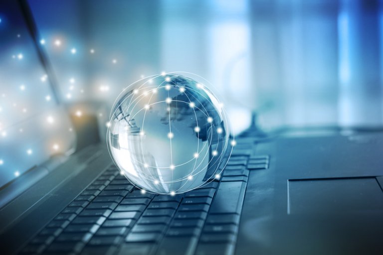 A transparent globe with interconnected dots sits on a laptop keyboard, representing virtual global connectivity. The background is blurred with a blue and white gradient, enhancing the theme of technology. Light points and lines underscore the digital network concept.