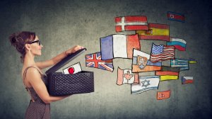A woman with glasses and a polka-dot dress holds an open box, from which colorful illustrated flags of various countries are emerging, including the USA, UK, France, Japan, and many others. She stands against a gray textured background, symbolizing global unity beyond government boundaries.