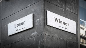 A corner of a gray stone building features two signs. The left sign reads "Loser" with an arrow pointing left, while the right sign beckons winners with an arrow pointing right. The signs appear to offer different directional choices.