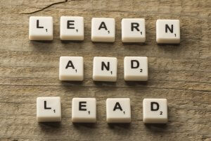Scrabble tiles arranged to spell "LEARN AND LEAD" on a wooden surface, symbolizing the path to leadership.