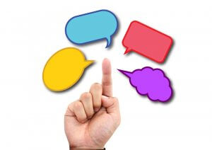 A hand pointing upward with its index finger extended, directed towards four colorful speech bubbles filled with quotes. The bubbles are in blue, red, yellow, and purple colors, floating above the finger against a white background.