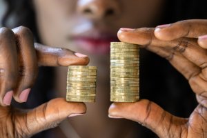Close-up of a person holding two stacks of coins in their hands. One stack is noticeably shorter than the other, subtly highlighting the issue of equal pay. The person is slightly out of focus in the background, emphasizing the coins.