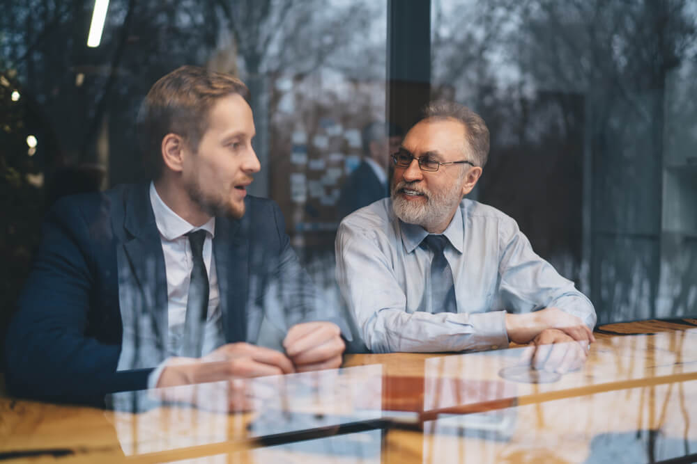 View,Through,Glass,Of,Cheerful,Mature,Businessman,Sitting,At,Table leadership