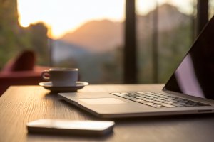 A close up of a cell phone, a laptop and a coffee cup