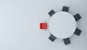 A round table with eight seats, one of which is noticeably different colored red in contrast to the seven black chairs surrounding it, signifying the leaders' position. The arrangement is on a light, minimalist background.