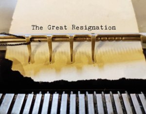 A close-up of a typewriter pressing the words "The Great Resignation" onto a sheet of paper. The image zeroes in on the mechanical intricacies and the typed text, underscoring the widespread wave of resignations.
