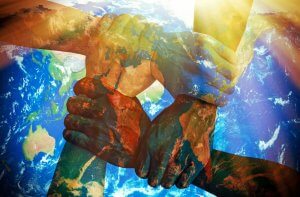 Four hands of different skin tones grip each other's wrists, forming a square. The hands are superimposed with a semi-transparent image of Earth from space, symbolizing global unity and humanitarian cooperation against a backdrop of sunlight.