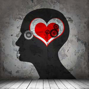 Silhouette of a human head on a textured wall, featuring a red heart with several interlocking gears inside it, symbolizing the connection between emotions and the mind's EQ. The background has a weathered, industrial appearance.