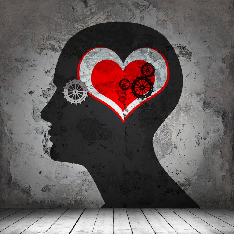 Silhouette of a human head on a textured wall, featuring a red heart with several interlocking gears inside it, symbolizing the connection between emotions and the mind's EQ. The background has a weathered, industrial appearance.