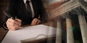 A person in a suit signs a document with a pen at a desk. The image is overlaid with a semi-transparent view of classical columns of a courthouse, symbolizing legal or official proceedings often associated with government jobs.