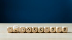 Wooden cubes are arranged to spell "IMPOSSIBLE" on a tabletop, except the cube with the letter 'I' is being rotated by a finger to form the phrase "IT'S POSSIBLE," symbolizing new career opportunities against a plain blue background.