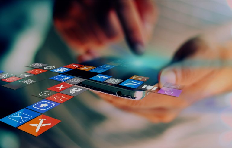 A person interacts with a smartphone, their fingers tapping on the screen. Various colorful app icons representing social media, messaging, and other utilities emanate from the device, suspended in mid-air, symbolizing digital connectivity and modern technology.