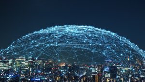 A city skyline at night is overlaid with a transparent digital grid dome, featuring interconnected nodes and lines, symbolizing global 5G communication and network connectivity. The buildings below are brightly lit, enhancing the futuristic atmosphere.