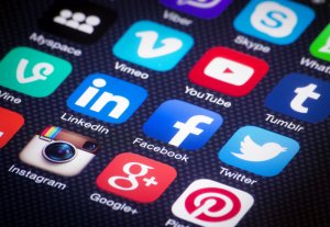 A smartphone screen displays a grid of colorful social media app icons on a black textured background. Visible icons include LinkedIn, Facebook, Instagram, Google+, Twitter, Pinterest, Myspace, Vimeo, YouTube, Skype, Vine, and Tumblr.