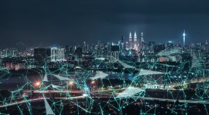 A nighttime cityscape is overlaid with a green digital network grid, connecting various points across the image. Tall skyscrapers and glowing city lights dominate the background, illustrating a bustling urban environment where remote work thrives, seamlessly interlaced with modern technology.