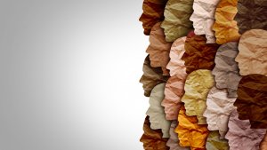 An illustration of diverse human profiles made from crumpled paper in various skin tones, overlapping and facing right against a light gray background. The left side of the image is blank, highlighting the beauty of diversity.