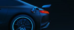 A sleek sports car is shown from the rear side, plugged into an electric charging station. The car's taillights are illuminated, and the image has a dark, modern background, highlighting the car's electric curves and design.