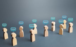 Wooden humanoid figures stand in two separate groups, each figure with a digital speech bubble above its head, suggesting career-related conversations or communication between the groups against a neutral gray background.