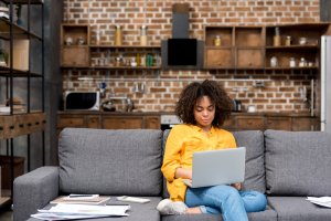 A young woman sitting on a couch, holding her laptop