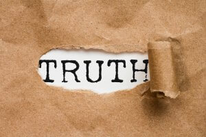 A piece of brown paper with a tear revealing the word "TRUTH" in bold, black letters underneath. The torn edge of the paper is curled up on the right side, emphasizing the hidden truth beneath.