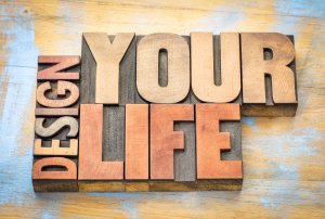 The image features large wooden block letters arranged to spell out "DESIGN YOUR LIFE" on a rustic, multicolored wooden background, serving as a devoted servant to your creative journey.