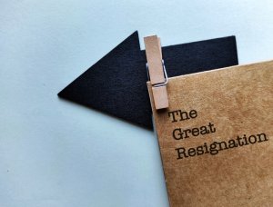A brown folder labeled "The Great Resignation" is clipped with a small wooden clothespin to a black arrow cutout, pointing to the left, against a light background, symbolizing changes in the workforce.