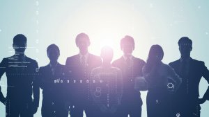 Silhouettes of six workers standing together against a light background with digital symbols and code overlay. The figures appear to be in a professional setting, with some wearing suits and others in business attire, suggesting teamwork or collaboration.