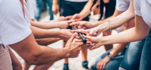 A group of people participating in an outdoor team-building activity where they collectively balance and lower a long, thin rod using just their fingertips. Everyone is engaged and focused, demonstrating teamwork and cooperation in this effective team-building exercise.