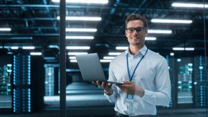 A man with glasses standing and holding a laptop