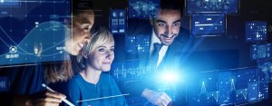 Three people collaborate in a dimly lit room filled with floating digital interfaces displaying charts, graphs, and data points. A bright blue light illuminates their faces, highlighting their focus on deciphering how many jobs are available in military, government, and technical sectors within the high-tech environment.