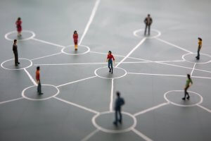 A conceptual image of social networking shows miniature figurines connected by white lines on a grey surface. Each figure stands in a circle, signifying connections and interactions, highlighting how people connect and engage within the network.