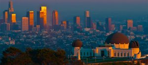 The image features the Griffith Observatory in the foreground with its white structure and domes. In the background, a cityscape of tall buildings is bathed in a golden sunset glow, showcasing a blend of natural elements and urban architecture where you can also *find great government jobs in California for free!*