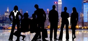 Silhouettes of six business professionals, three men and three women, posed against a backdrop of a lit-up city skyline at night. The reflective ground beneath them adds a glossy effect to the image, mirroring discussions of the pros and cons of government jobs in the USA.