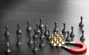 A red horseshoe magnet attracting a group of gold chess pawns, symbolizing the government's influence, while several black chess pawns are scattered on a gray surface in the background.