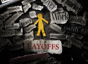 A cut-out figure of a person stands amidst a chaotic collage of newspaper clippings with words like "layoff," "struggle," "economic ruin," and "fear" prominently displayed, reflecting themes of job loss and economic hardship.