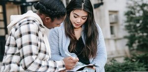 Two female student discussing something written in a book