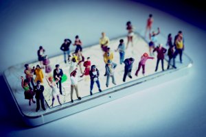 A photograph of a smartphone displays a grid on its screen, over which miniature figurines of people in various poses and attire are arranged in rows and columns, resembling a meticulously organized government assembly.