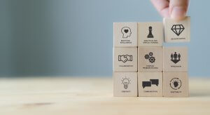 A hand arranges wooden blocks labeled with essential career skills: Emotional Intelligence, Analytical and Critical Thinking, Decision Making, Collaboration, Complex Problem Solving, Persuasion, Creativity, Communication, Adaptability.