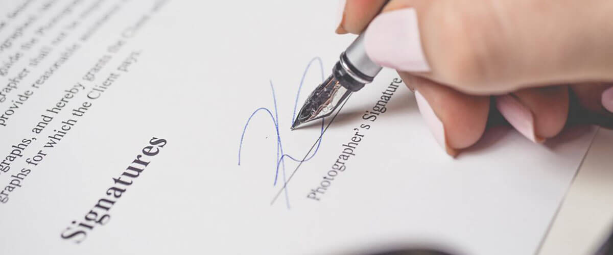 A picture showing a hand holding a pen signing a document
