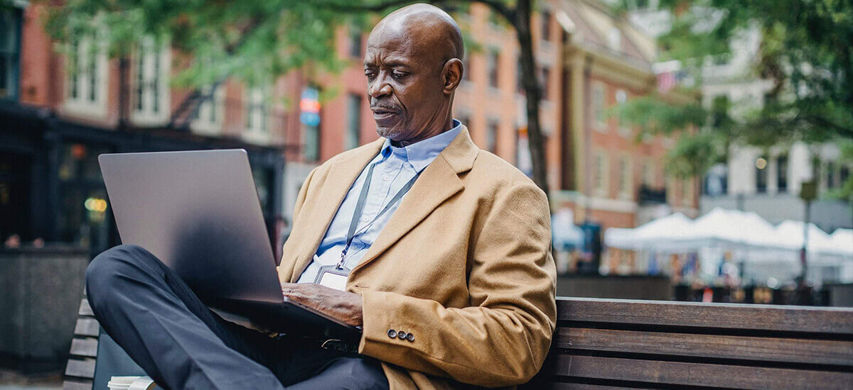 A man pressing a laptop while sitting on a bench