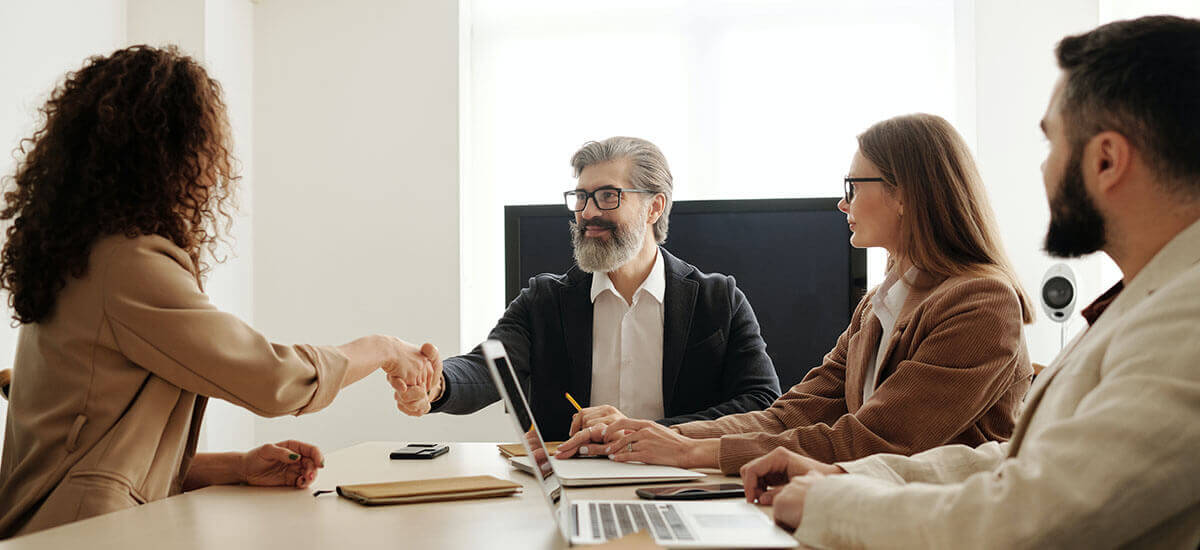 A woman shaking hands with an elderly man in front of two other people in a conference room