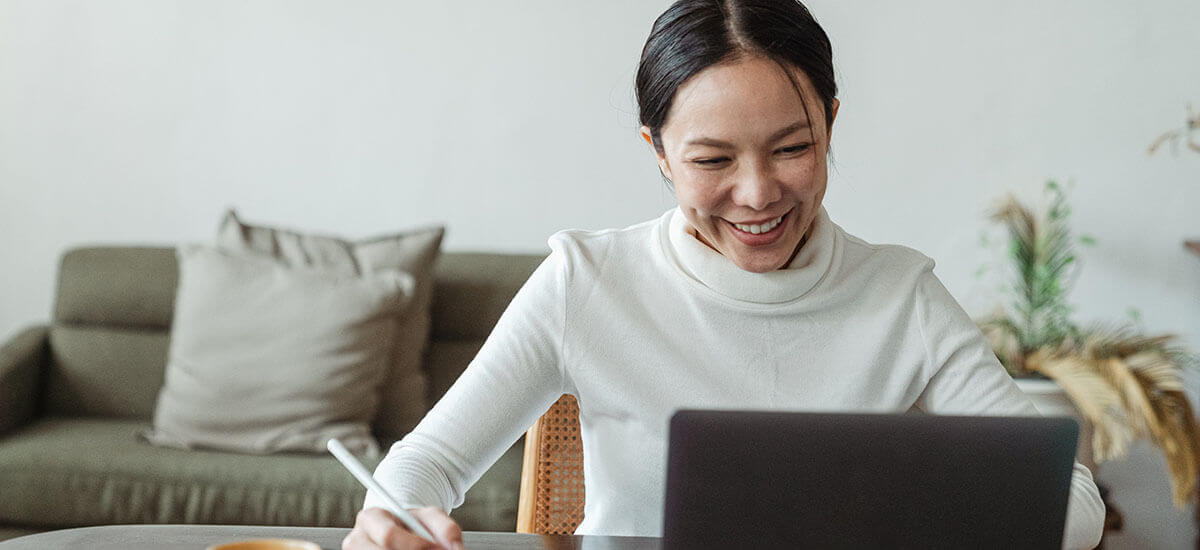 A happy female worker holding a pen in front of a laptop