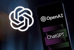 A smartphone displays the logos of OpenAI and its famous AI language model, ChatGPT, on its screen. In the background, the OpenAI logo is prominently shown, emphasizing both the brand and ChatGPT's prominence.