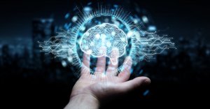 A person’s outstretched hand with a digital, glowing brain hologram floating above it, surrounded by a network of connecting lines and circuits symbolizing AI and advanced technology. The background is dark and blurred.