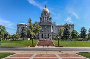 A large, ornate building with a golden dome and a wide staircase leading to the entrance, dedicated to public service, surrounded by trees and a well-manicured lawn under a blue sky. The building features columns and intricate architectural details.