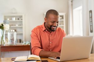 A man smiling while using his laptop for communicating
