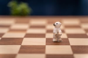 A small polar bear figurine stands upright on a chessboard, embodying leadership. The foreground is sharply in focus, highlighting the bear and the surrounding chessboard squares, while the background is blurred with indistinct shapes.