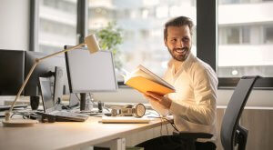 A man happily working with a book in front of his desk