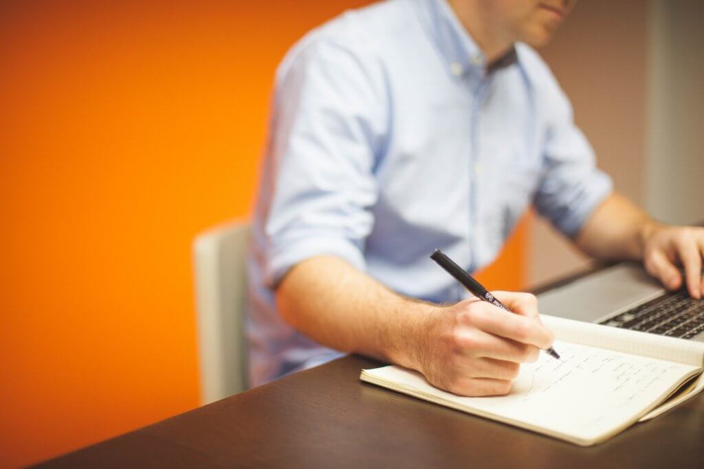 Someone writing in front of a laptop